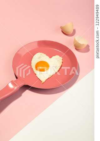 Creative idea with a pink frying pan and egg in heart shape on white and pink background. Minimal food and love concept. Breakfast idea for Valentine's day and romantic morning. 122949489