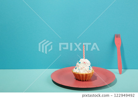 Delicious birthday cupcake with candle on pink plate on blue background. Creative photo 122949492