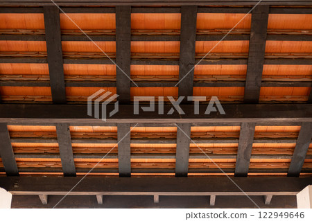 A view from inside a wooden pavilion, with dark wooden beams and terracotta roof tiles 122949646