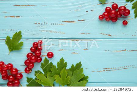 Ripe red currant with green leaves on blue wooden background. Top view. Ripe red currant with green leaves on blue wooden background. Top view. 122949723