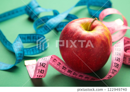 Diet concept with apple and measuring tapes, on a green background. 122949740