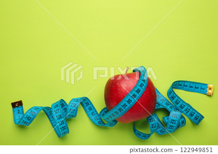 Diet Concept with apple and blue measuring tape, on green background. Diet Concept with apple and blue measuring tape, on green background. 122949851