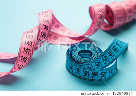 Blue and pink plastic measure tape with metric scale over on color blue background. Blue and pink plastic measure tape with metric scale over on color blue background. 122949854