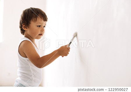 Close-up of a little boy painting a wall. Cute toddler is drawing on the wall. A carefree child is having fun at home. 122950027