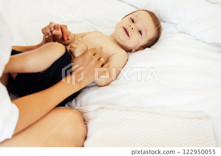 Close-up of a child portrait of a cute little boy lying on a white sheet. Sweet toddler is having fun with his mom in the bedroom at home. 122950055