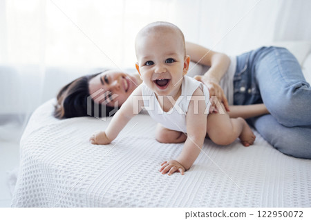 Pretty infant in a white bodysuit with his mom on a light background. Motherhood concept. Pretty infant in a white bodysuit with his mom on a light background. Motherhood concept. 122950072
