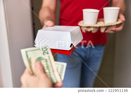 delivery man in red uniform giving food box and paper coffee cups to customer and taking payment at home delivery man in red uniform giving food box and paper coffee cups to customer and taking payment at home 122951136