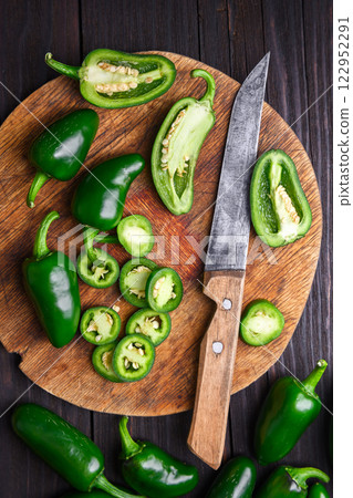 Sliced green jalapeno hot peppers on round wooden cutting board 122952291