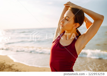 Modern young woman doing yoga on beach at sunrise. Concept of an active lifestyle, yoga or fitness. 122953259