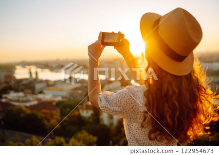 Young Woman on vacation using mobile phone to take photo of sunset of city. Rest, lifestyle concept. Young Woman on vacation using mobile phone to take photo of sunset of city. Rest, lifestyle concept. 122954673