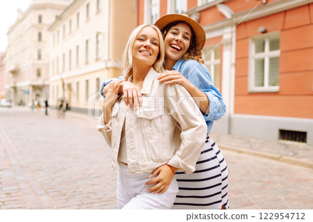 Happy women walk along city streets on sunny day. Young girlfriends having fun outdoors. Lifestyle. 122954712