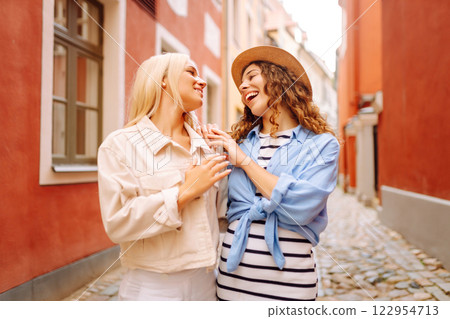 Happy women walk along city streets on sunny day. Young girlfriends having fun outdoors. Lifestyle. Happy women walk along city streets on sunny day. Young girlfriends having fun outdoors. Lifestyle. 122954713