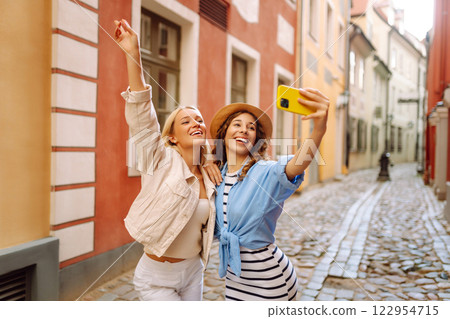 Happy female tourists in casual clothes walk along streets of Europe, take selfies. Active lifestyle Happy female tourists in casual clothes walk along streets of Europe, take selfies. Active lifestyle 122954715