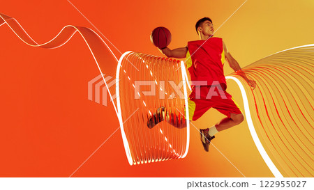 Sport collage. Basketball athlete in powerful jump in motion, holding ball with glowing light trails emphasizing movement against fiery background. 122955027