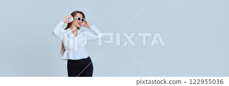 Banner. Young woman, with energetic facial expression, wearing white headphones and sunglasses, dancing, enjoying music against white studio background. 122955036