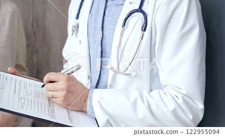 Doctor and patient. Close-up of a doctor's hand taking notes on a clipboard with a woman in the background. Medicine and Health care 122955094