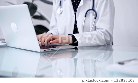 Doctor woman is typing on laptop computer at glass table in clinic, horizontal view. Medicine and pharmacy concept Doctor woman is typing on laptop computer at glass table in clinic, horizontal view. Medicine and pharmacy concept 122955102
