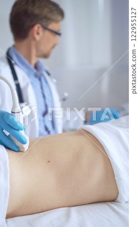 Doctor man wearing blue protective gloves is using ultrasound equipment on the back of a patient, woman. Medicine service 122955127