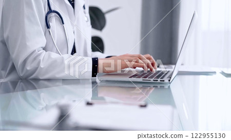Doctor woman is typing on laptop computer at glass table in clinic, horizontal view. Medicine and pharmacy concept 122955130