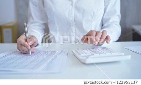 Businesswoman with white blues calculating finance with calculator and taking notes at office table. Audit and taxes Businesswoman with white blues calculating finance with calculator and taking notes at office table. Audit and taxes 122955137