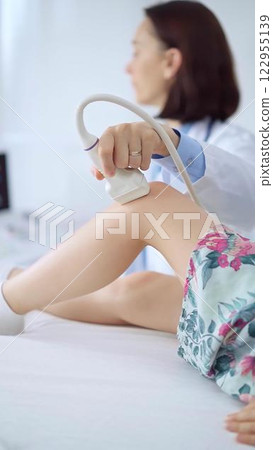 Doctor and kid patient. Orthopedist performing ultrasound examination on a child's knee in a clinic. Medicine and health care Doctor and kid patient. Orthopedist performing ultrasound examination on a child's knee in a clinic. Medicine and health care 122955139