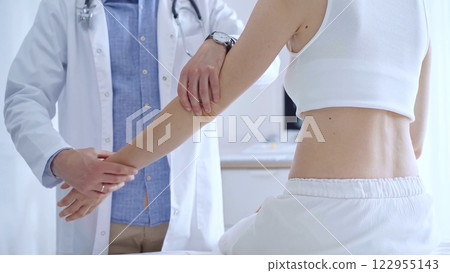 Doctor man examines a patient's elbow during a medical consultat 122955143