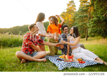 Stylish friends enjoy sunny day on beautiful green meadow. Vacation, friendship or holliday concept. 122955188