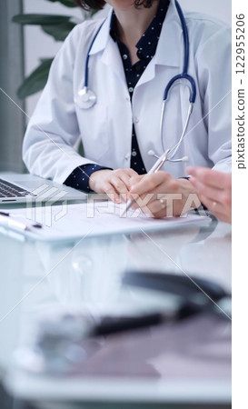 Doctor and patient. Female physician is sitting at the glass table, listening a senior man and writing medication history records. Medicine concept 122955206