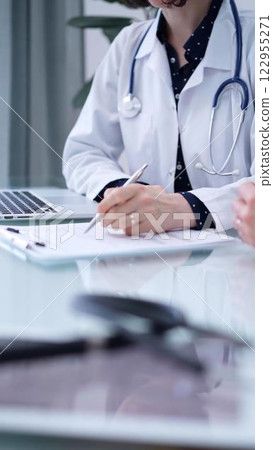 Doctor and patient. Female physician is sitting at the glass table, listening a senior man and writing medication history records. Medicine concept 122955271