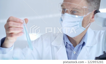 Scientist researcher with protective glasses and mask examining lab tube with a green fluid. Microbiology and science concept 122955281