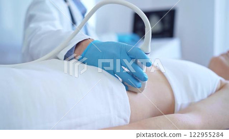 Doctor man wearing a blue medical gloves using an ultrasound equipment on a female patient lying down in clinic cabinet, close up view. Medicine concept 122955284