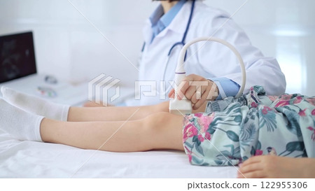 Doctor and kid patient. Orthopedist performing ultrasound examination on a child's knee in hospital. Medicine 122955306