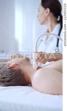 Doctor woman performing neck ultrasound exam on male patient. Medicine service concept Doctor woman performing neck ultrasound exam on male patient. Medicine service concept 122955319