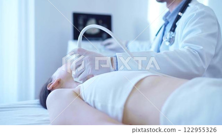 Doctor man with white medical gloves is using ultrasound machine to examine neck of female patient lying down in clinic. Medicine concept 122955326