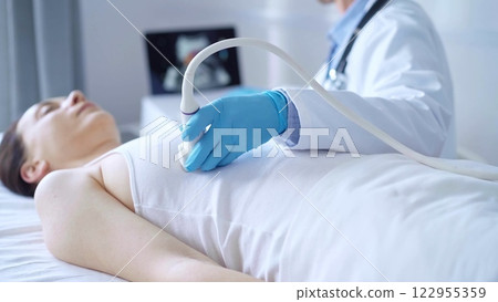 Doctor man, wearing white medical gloves, is using ultrasound equipment on the breast of a female patient. Female breast cancer prevention. Medicine concept 122955359