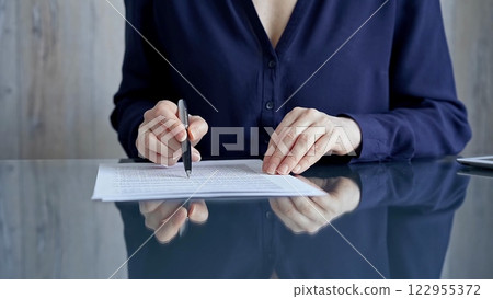 Businesswoman in dark blue blouse signing contract at the table. Close-up of a male executive signing a legal document on a glass desk. Business people concept 122955372