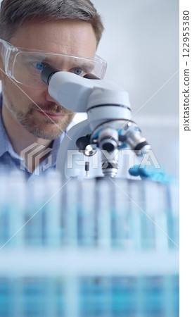 Man scientist with protective glasses and gloves is using microscope in laboratory, vertical portrait of researcher. Microbiology science concept 122955380
