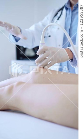 Male doctor with white medical gloves using ultrasound equipment on the knee of a female patient. The results on a monitor in the background. Medicine concept Male doctor with white medical gloves using ultrasound equipment on the knee of a female patient. The results on a monitor in the background. Medicine concept 122955387