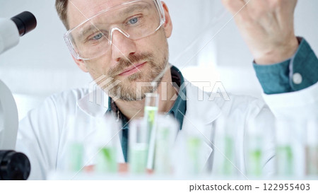 Man with safety glasses is working with lab tubes using a pipette in a modern laboratory, close-up of researcher. Science and medicine 122955403