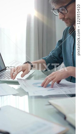 Entrepreneur wearing green shirt and glasses is working at laptop with data analysis charts. Vertical business portrait 122955410