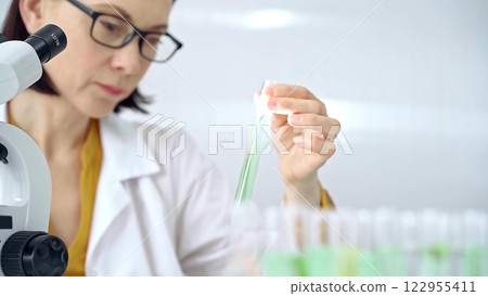 Scientist examining lab tube with a green fluid. Microbiology and science concept Scientist examining lab tube with a green fluid. Microbiology and science concept 122955411