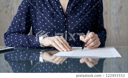 Businesswoman is signing corporate contract at her office desk in formal dark blue blouse with polka dots. Business people concept 122955552