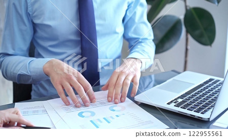 Businessman and woman analyzing data at glass desk beside a laptop in modern office, close up view. Business concept 122955561