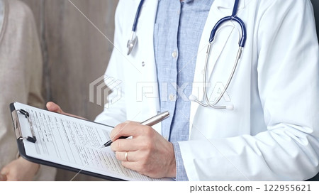 Doctor and patient. Close-up of a doctor's hand taking notes on a clipboard with a woman in the background. Medicine and Health care 122955621