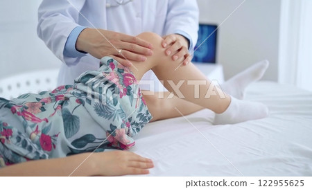 Doctor and kid patient. Orthopedist examining girl's knee in medical clinic. Medicine and health care 122955625