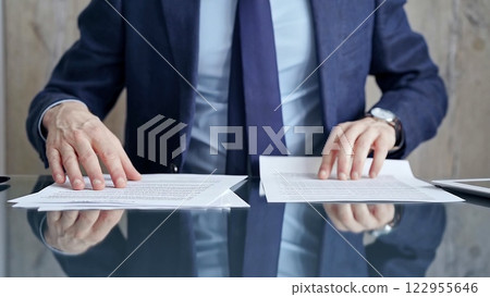 Businessman reviewing documents at office desk. Close-up of a professional man's hands examining paperwork with pen and tablet in sight. Business people concept Businessman reviewing documents at office desk. Close-up of a professional man's hands examining paperwork with pen and tablet in sight. Business people concept 122955646