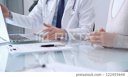 Doctor is consulting patient in modern fair clinic. Healthcare professional discusses medical information with a woman, pointing into the laptop computer monitor. Medicine concept 122955648