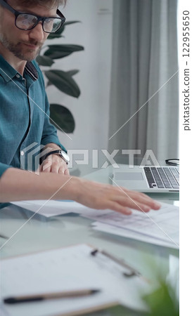 Businessman auditor wearing green shirt and glasses is working with laptop computer and financial papers. Vertical business portrait Businessman auditor wearing green shirt and glasses is working with laptop computer and financial papers. Vertical business portrait 122955650