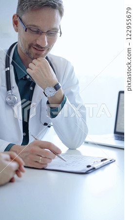 Doctor and a patient. The physician, wearing a white medical coat over a green shirt, gesturing with his hands during a consultation in the clinic. Medicine concept Doctor and a patient. The physician, wearing a white medical coat over a green shirt, gesturing with his hands during a consultation in the clinic. Medicine concept 122955679