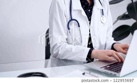 Doctor woman is typing on laptop computer at glass table in clinic. Medicine and pharmacy concept Doctor woman is typing on laptop computer at glass table in clinic. Medicine and pharmacy concept 122955697
